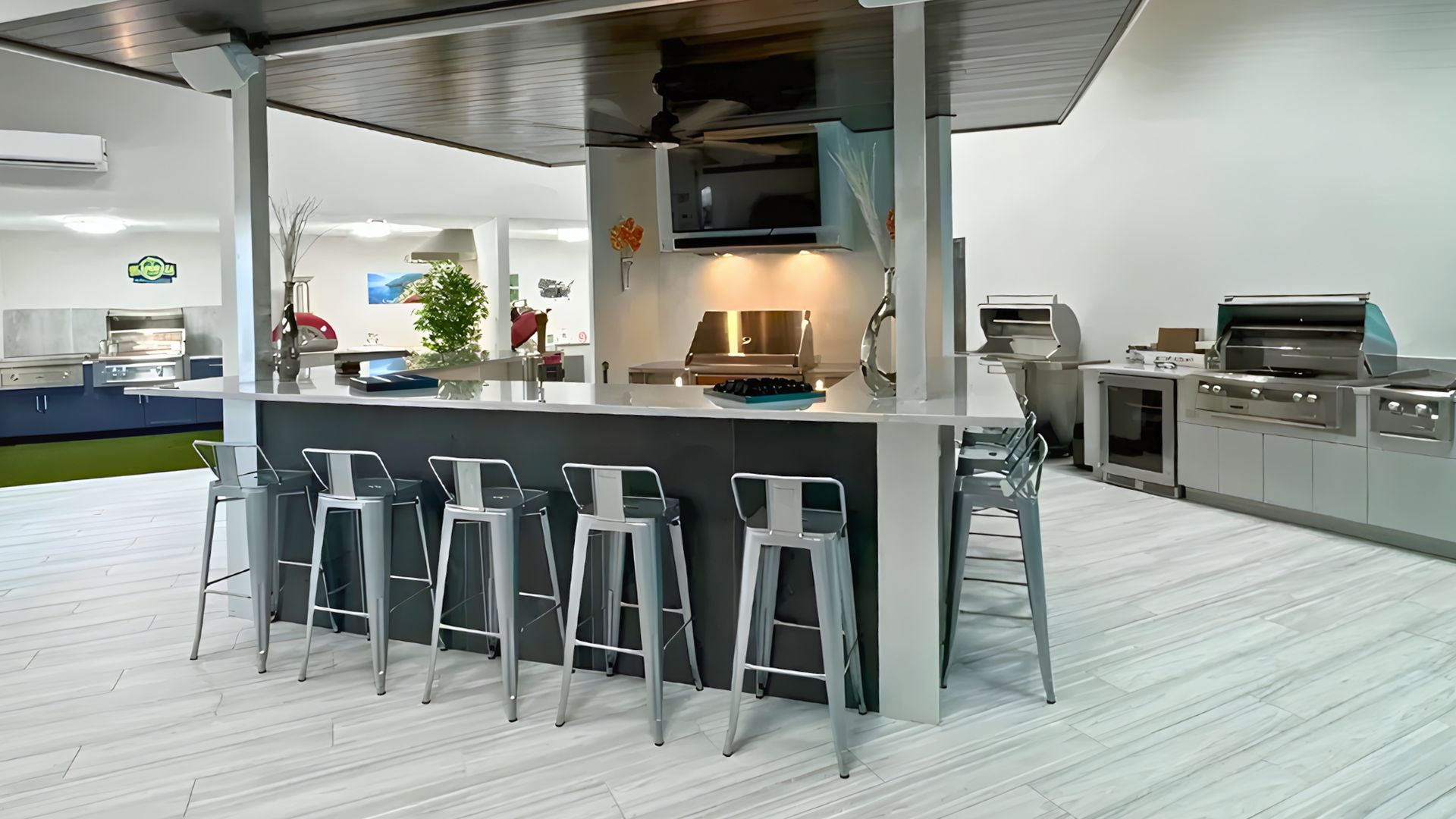 A modern indoor kitchen island with a dark countertop and five metal stools, featuring a range hood and stainless grills.