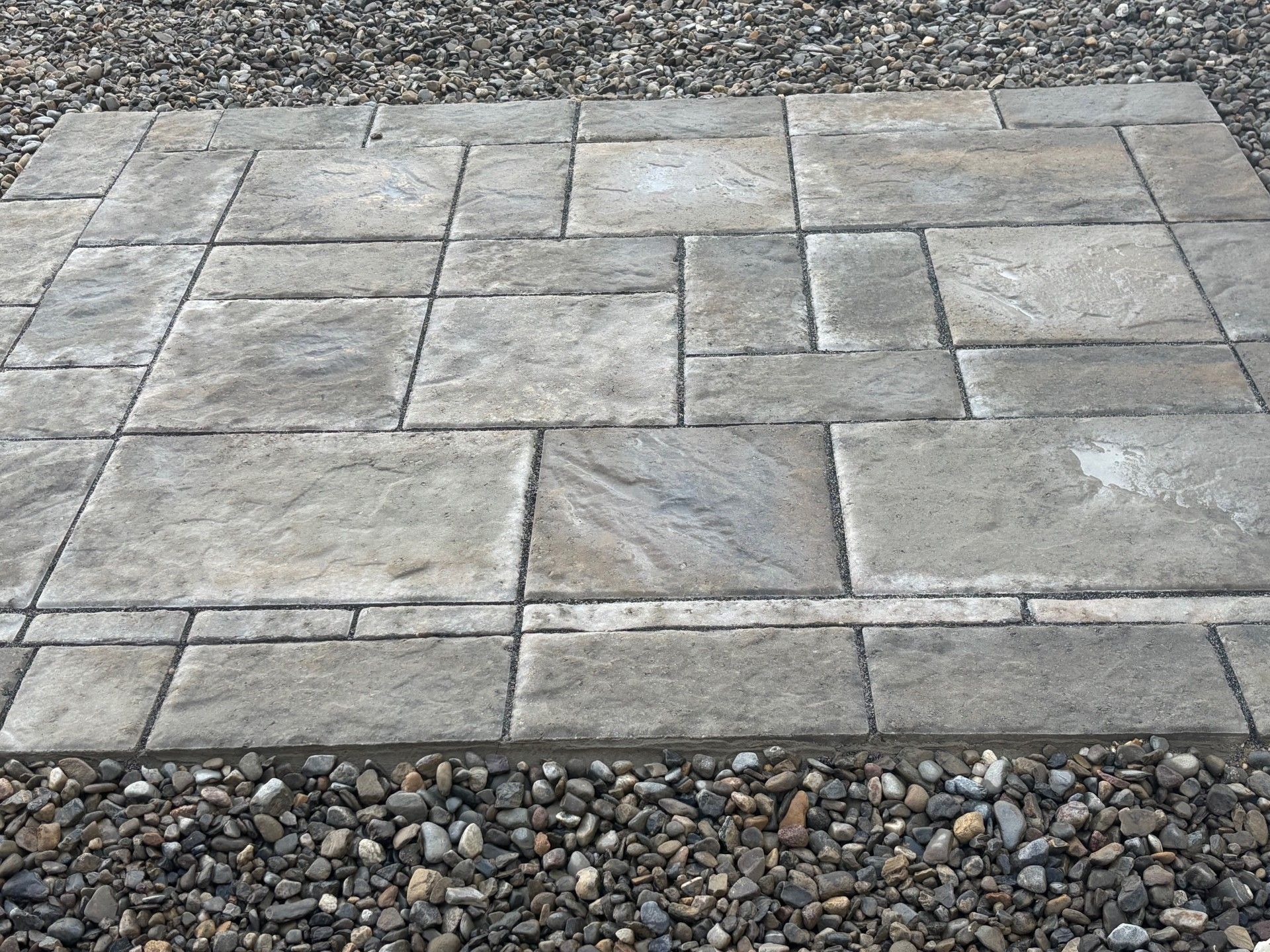 A square stone patio display featuring multi-sized, grey, weathered-texture pavers laid in an interlocking pattern.