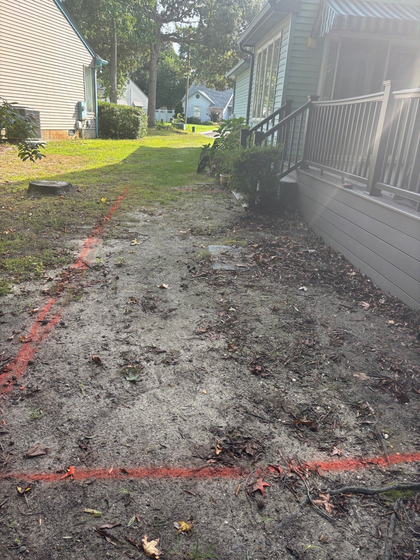 An outdoor space beside a house features a patch of dirt marked with red lines, likely indicating a planned construction.