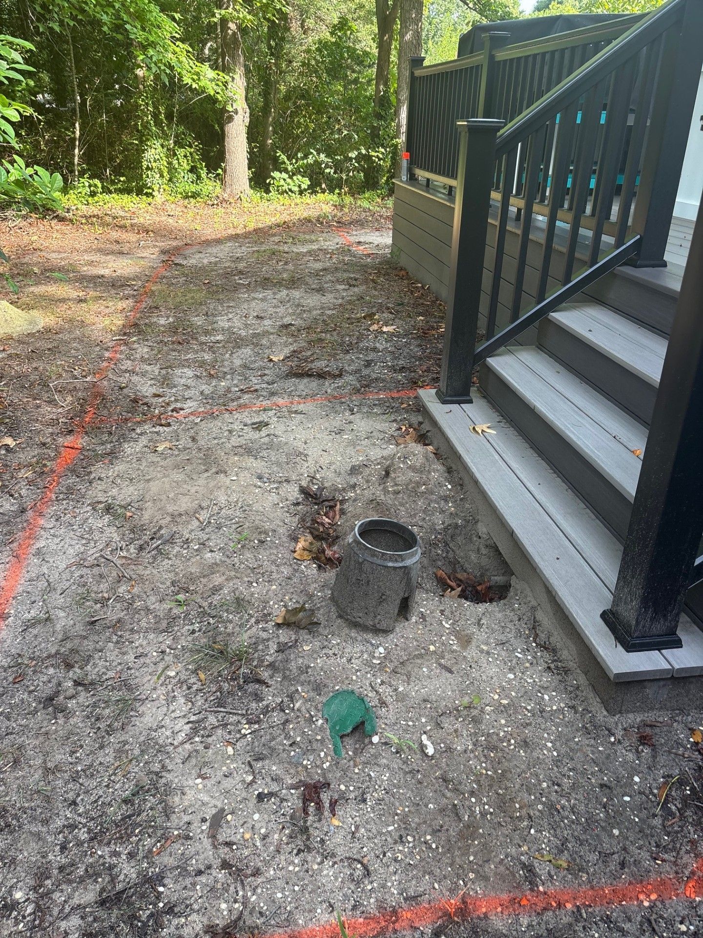 An outdoor space with orange construction flags marking a patch of sandy soil next to a dark gray deck and stairs.