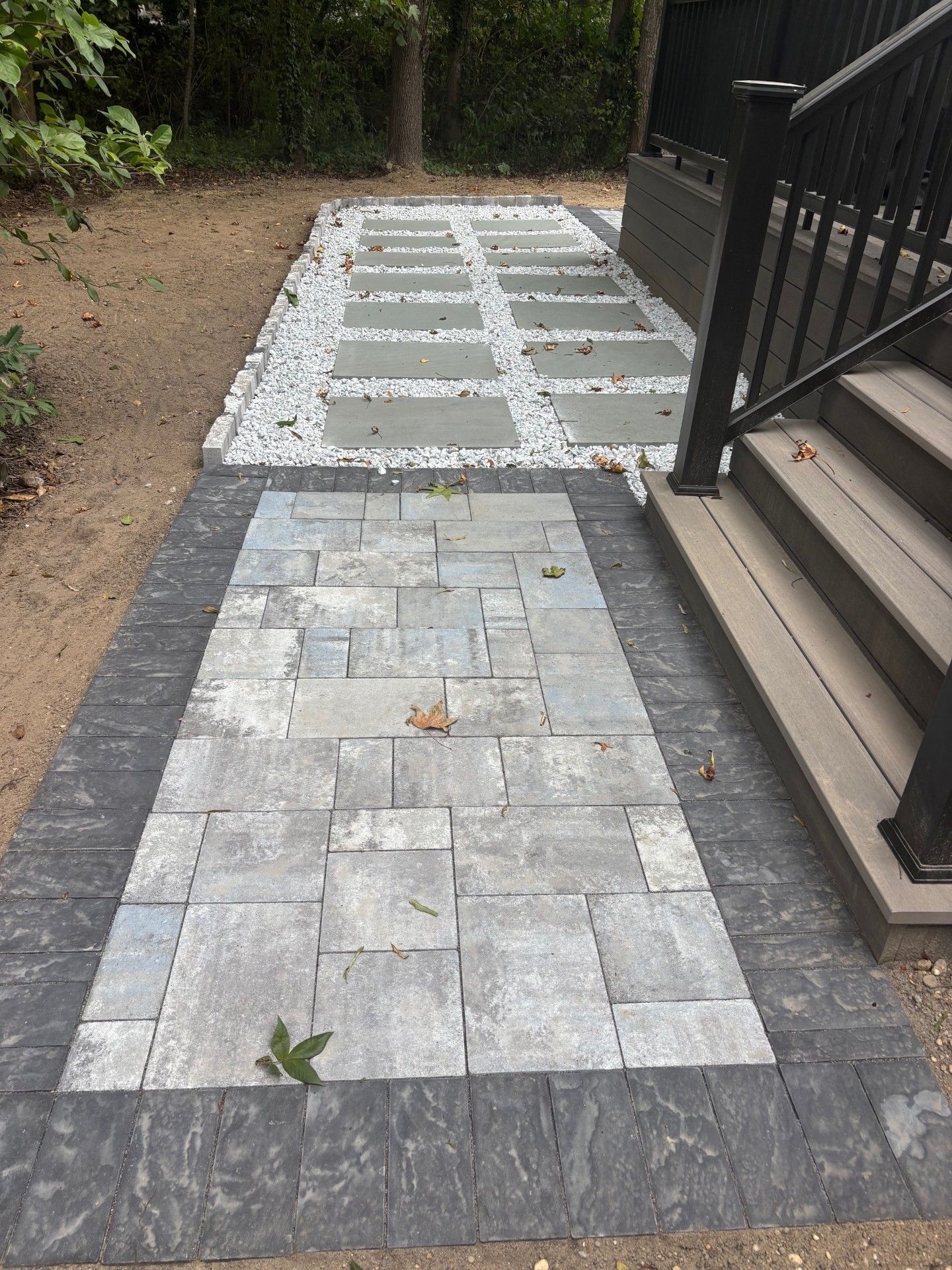 A backyard stone pathway featuring a rectangular block-paver section and a grid of large pavers set in white gravel.