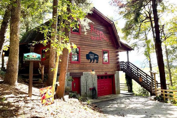 A large wooden house with a red garage door is surrounded by trees.