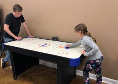 A boy and a girl are playing air hockey on a table.