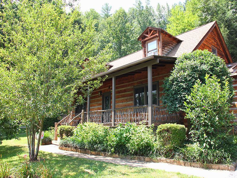 A large log cabin with a large porch is surrounded by trees and bushes.