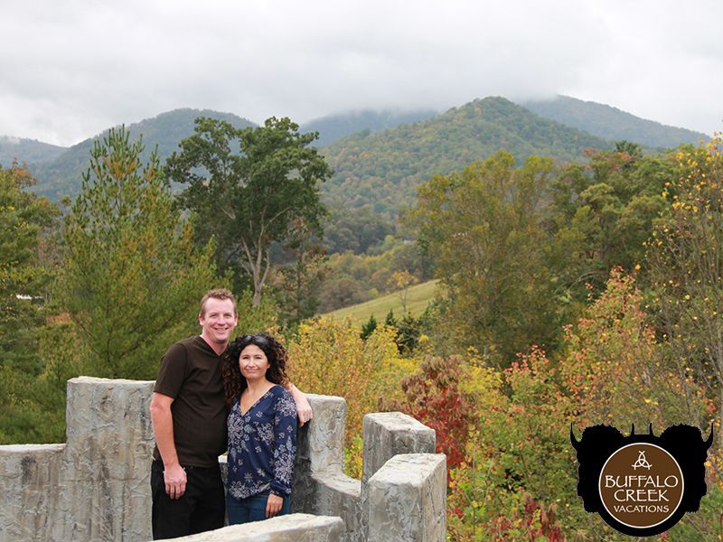 A man and a woman are posing for a picture with mountains in the background.