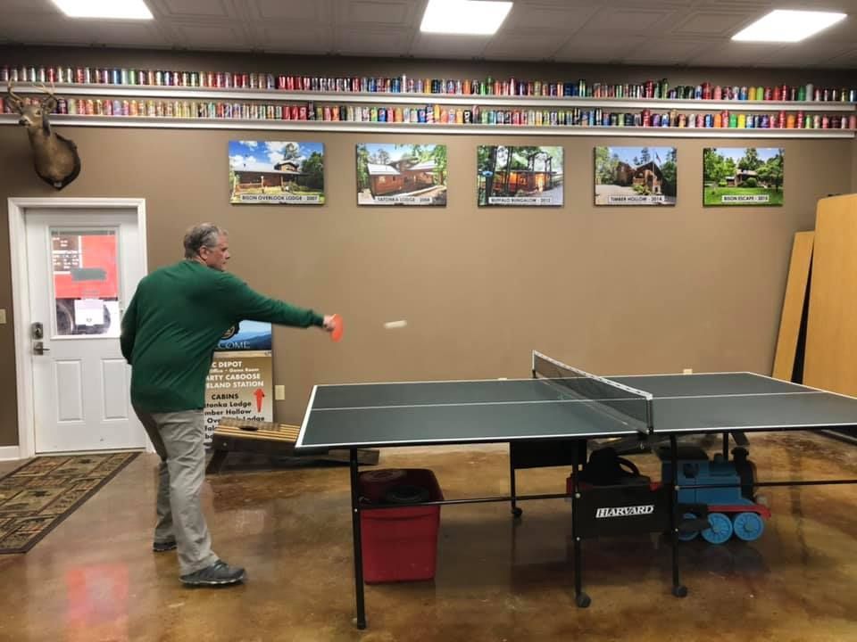 A man is playing ping pong in a room with pictures on the wall.