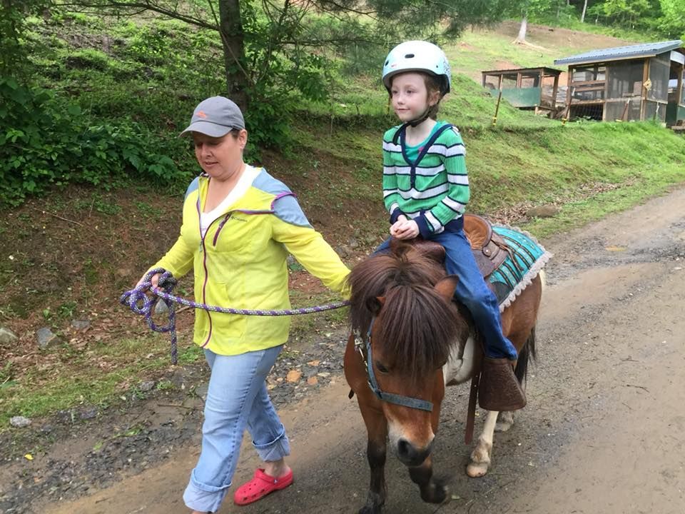 A woman is helping a young boy ride a pony on a dirt road.