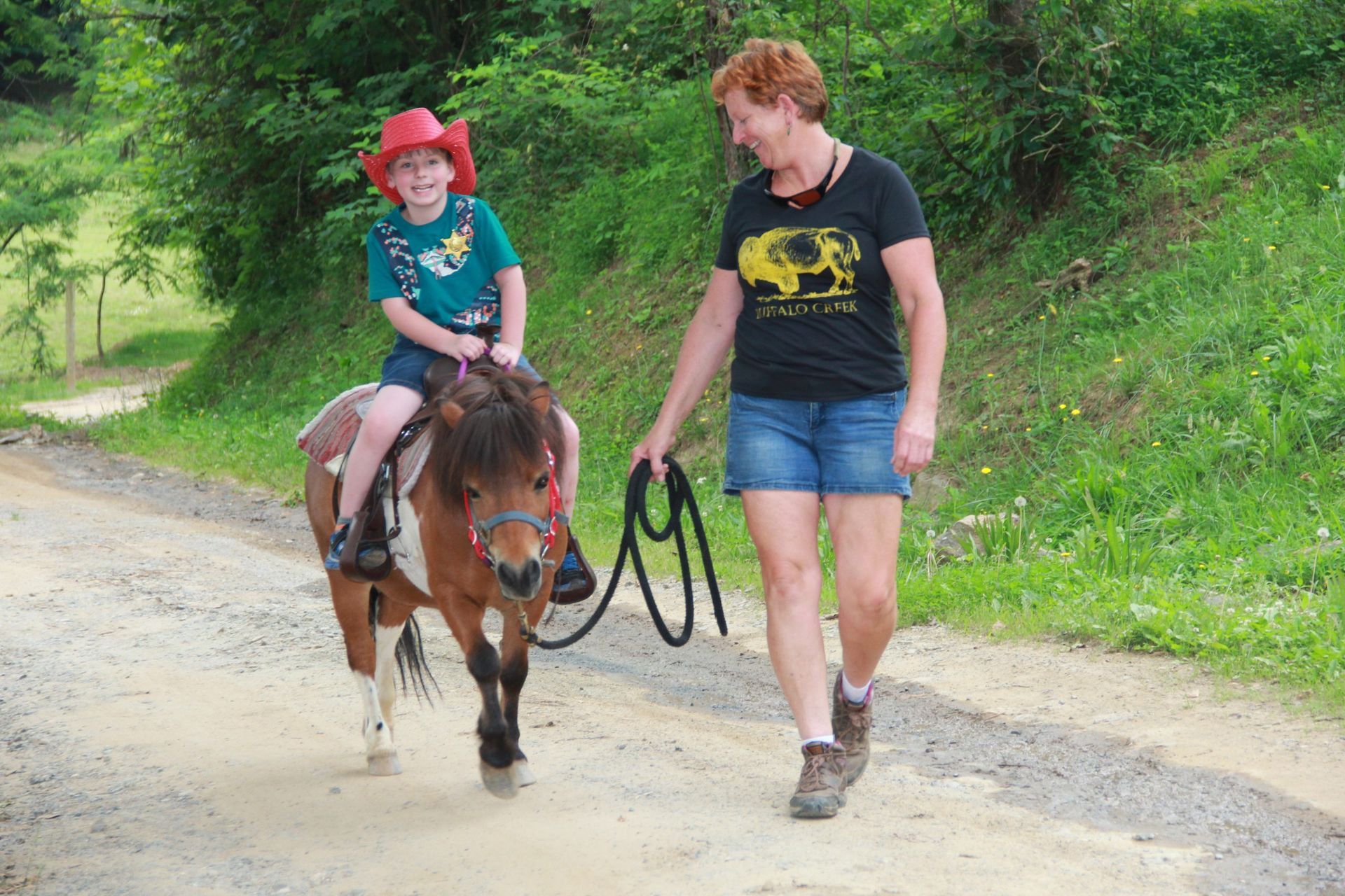A woman is walking a child on a pony down a dirt road.