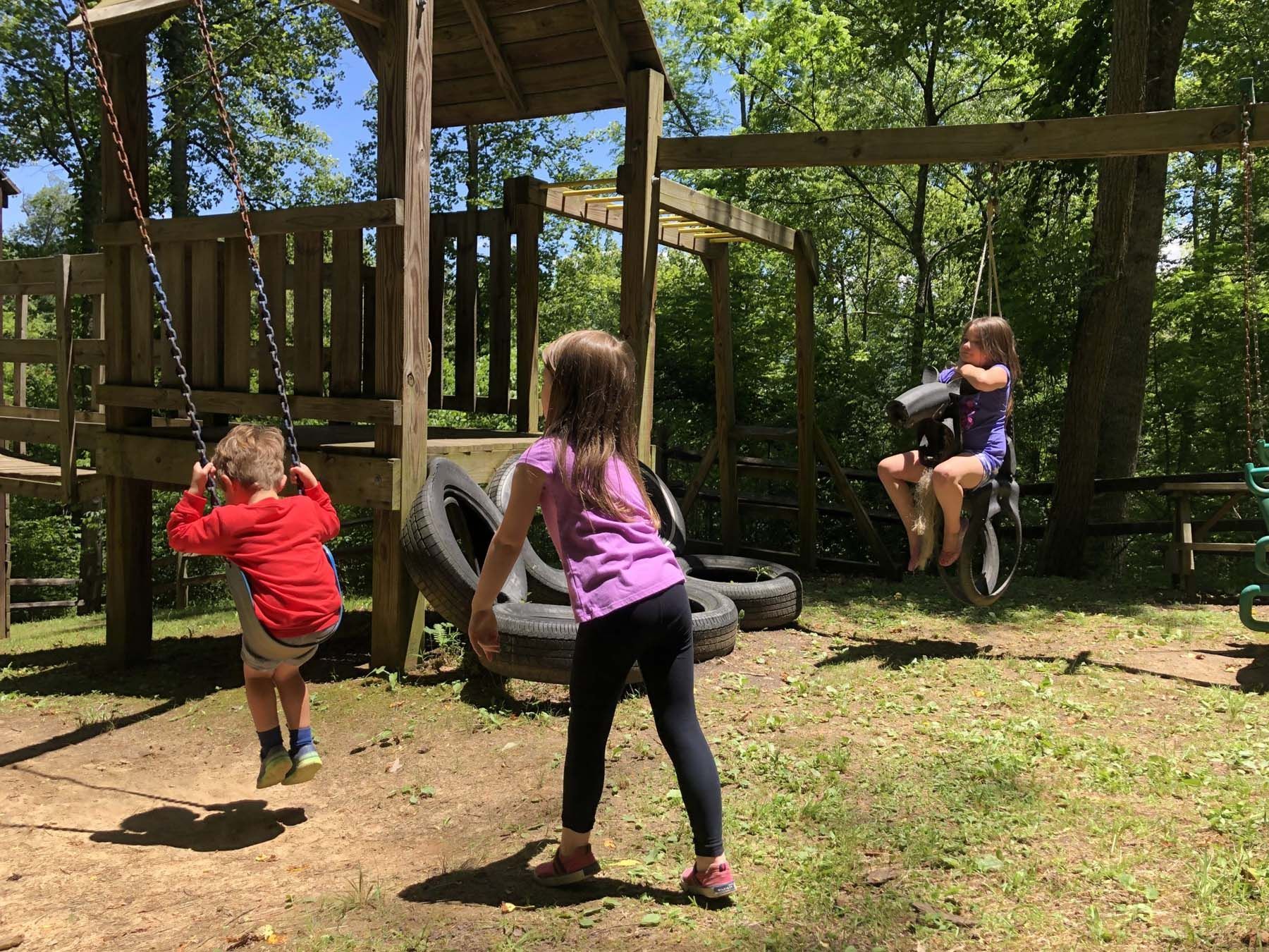 Three children are playing on tire swings in a playground.