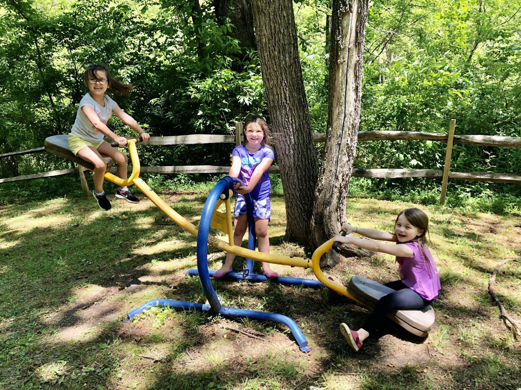 Three young girls are playing on a seesaw in a park.