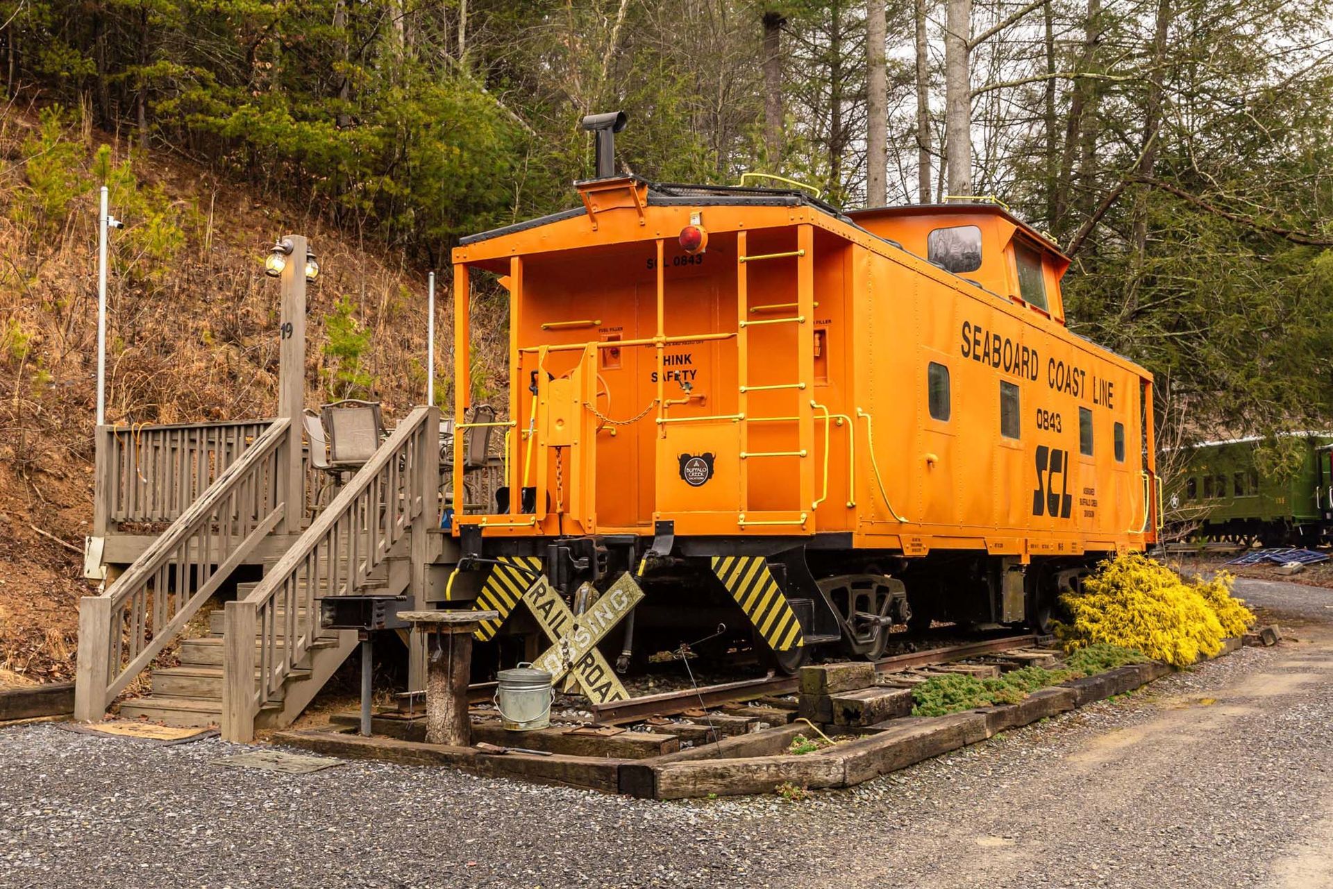 A yellow train car is parked next to a wooden deck and stairs.