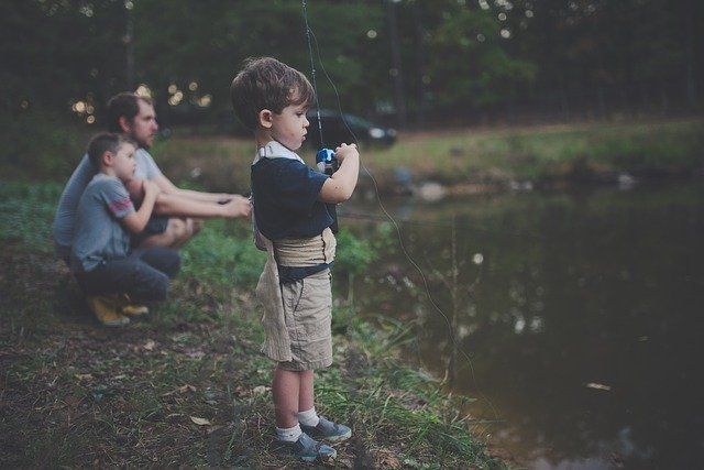 A little boy is fishing in a pond while his father watches.