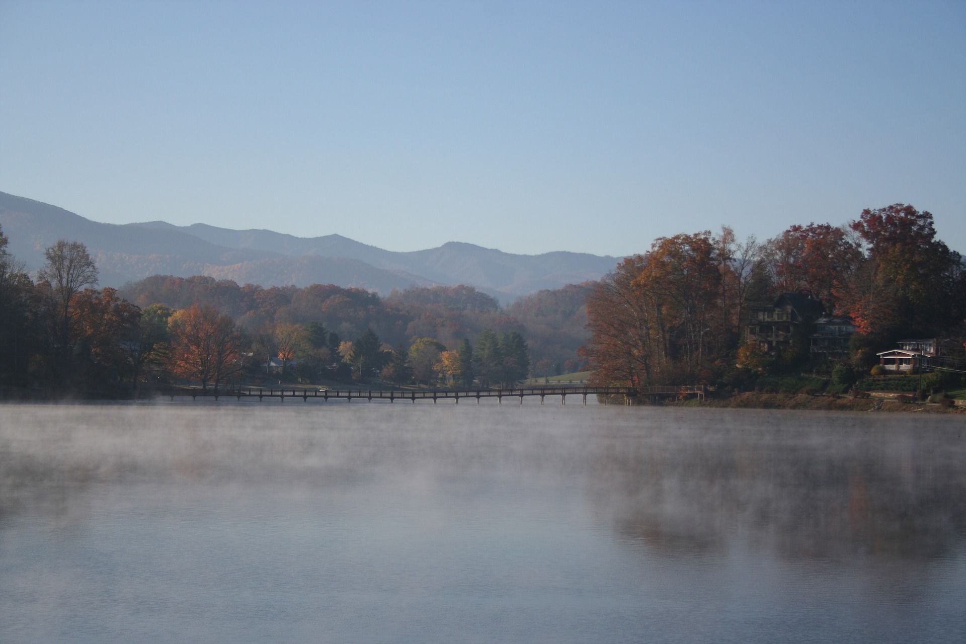 A foggy lake with mountains in the background and trees on the shore.