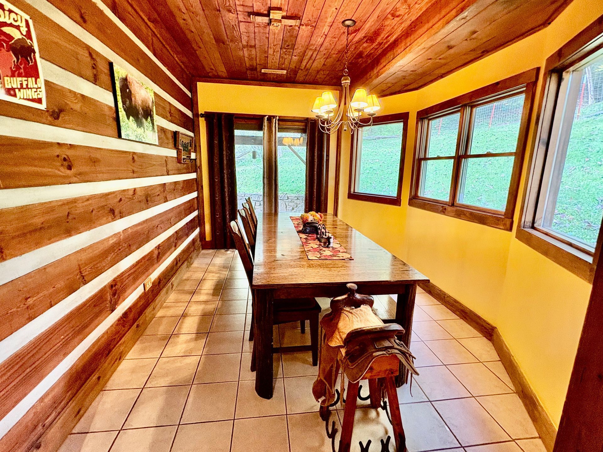 Dining room with log siding, wood ceiling, table set for meal, saddle on chair.