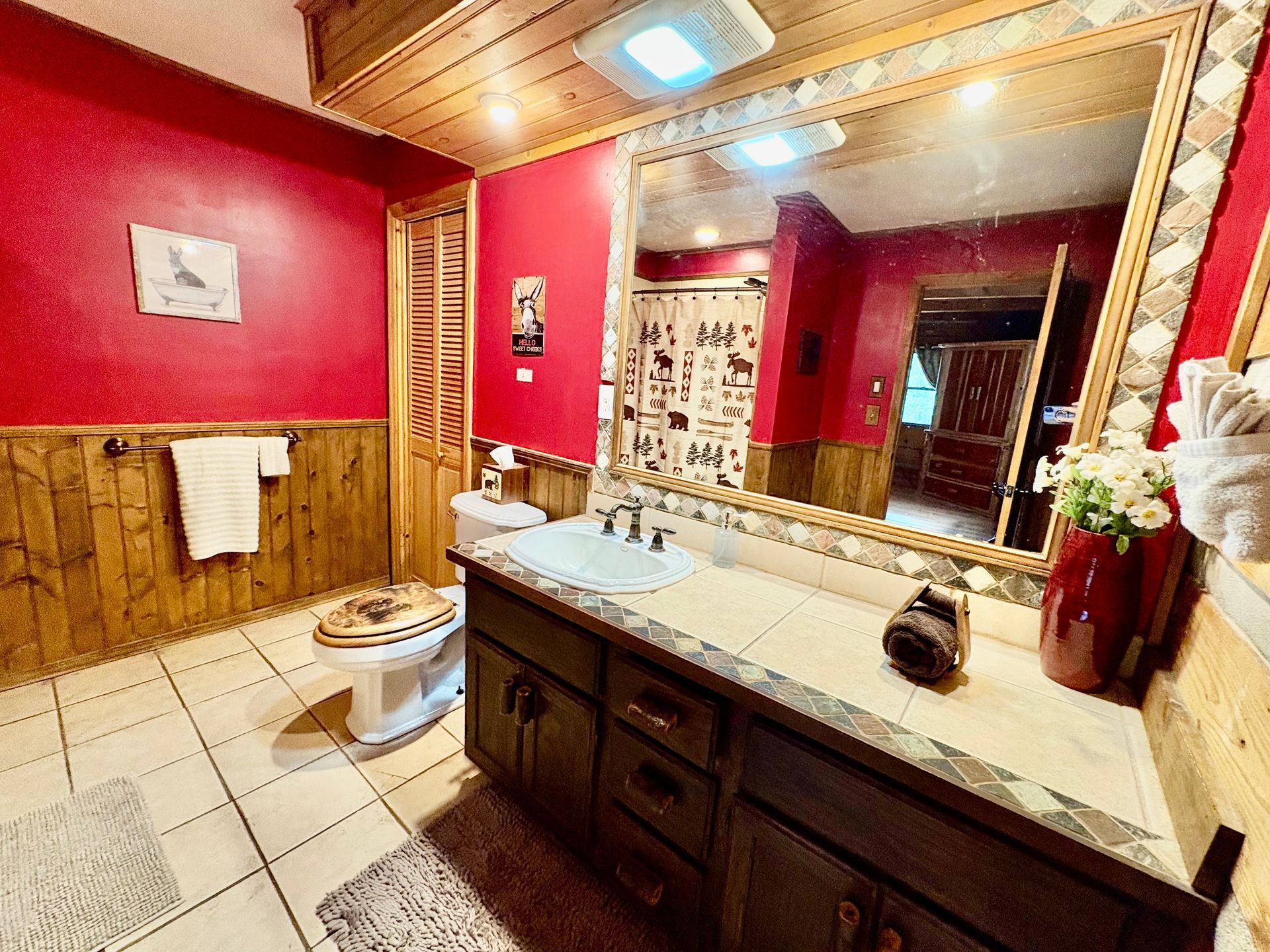 Rustic bathroom with red walls, wood paneling, large mirror, and vanity.