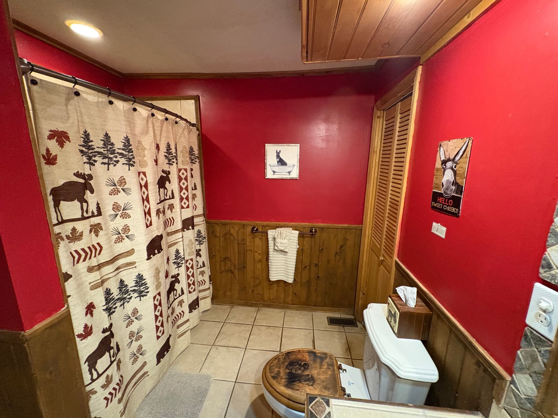 Bathroom with red walls, wooden trim, a rustic shower curtain, and a wood toilet seat.