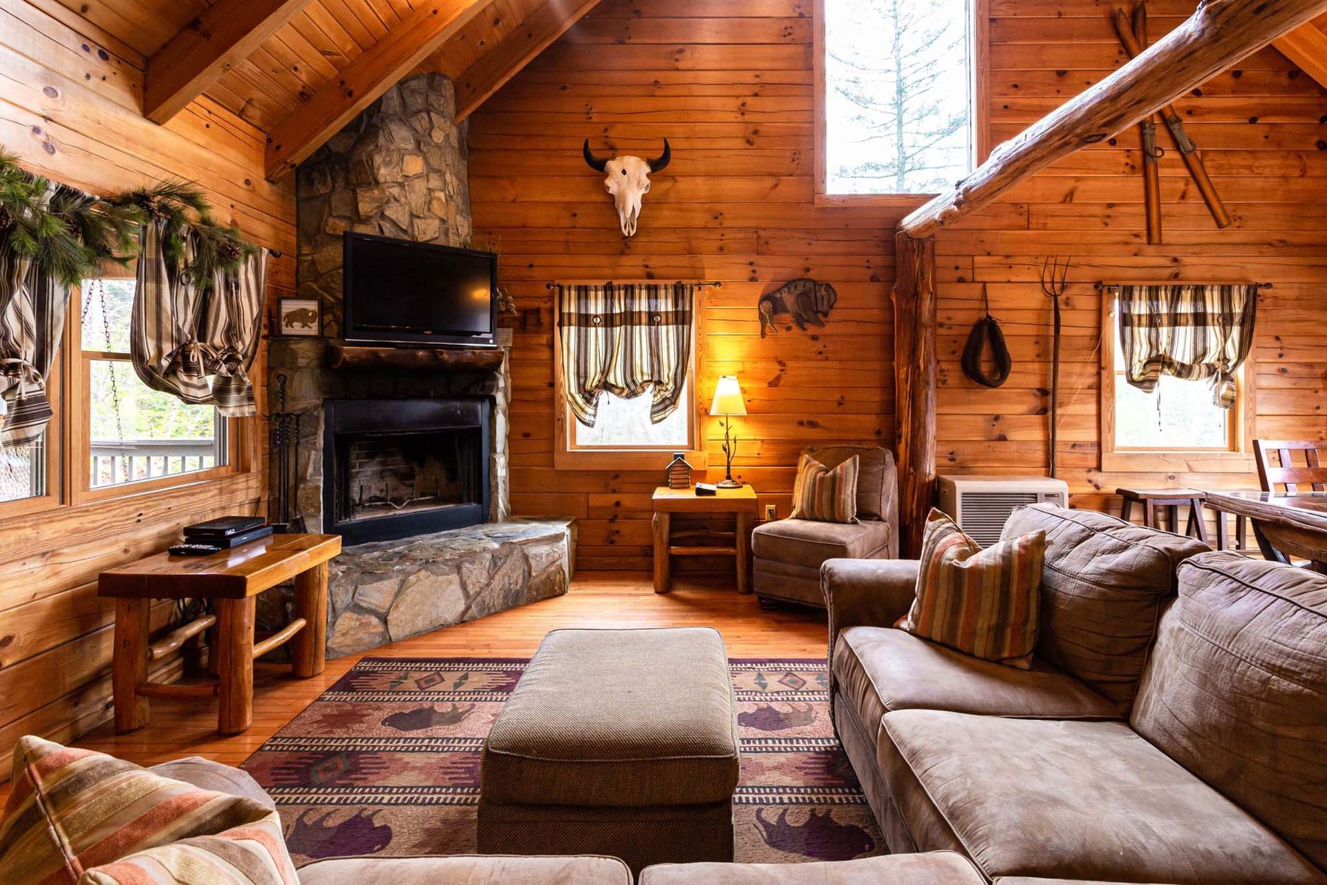 A living room in a log cabin with a couch , chairs , fireplace and television.