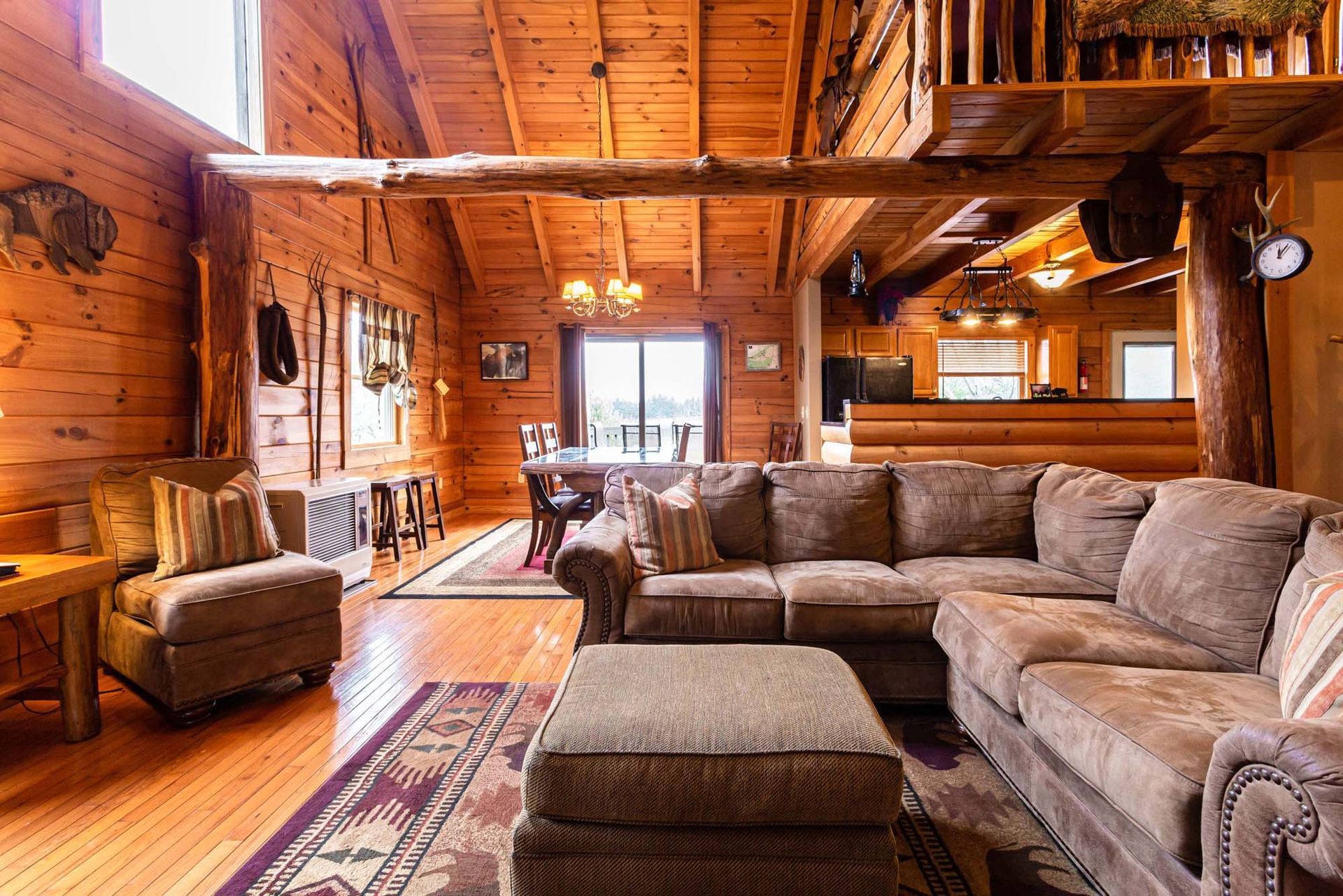 A living room in a log cabin with a sectional couch , chairs , and ottoman.