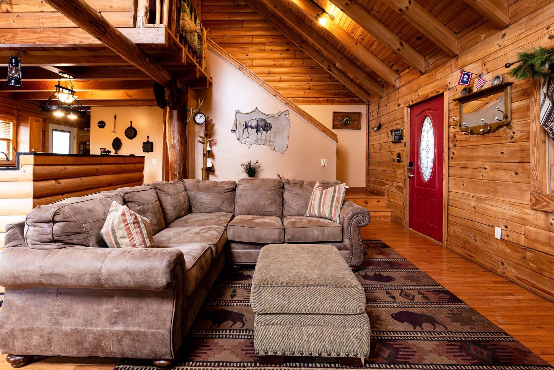 A living room in a log cabin with a sectional couch and ottoman.