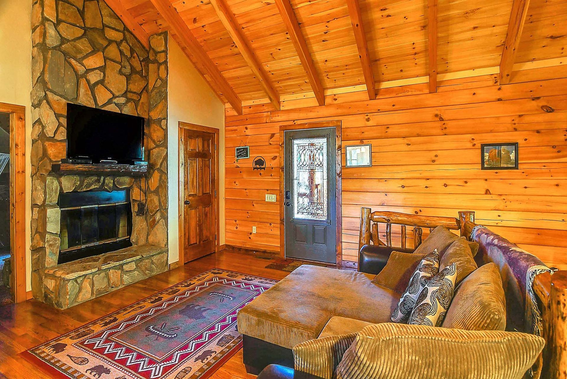 A living room in a log cabin with a couch , fireplace and television.