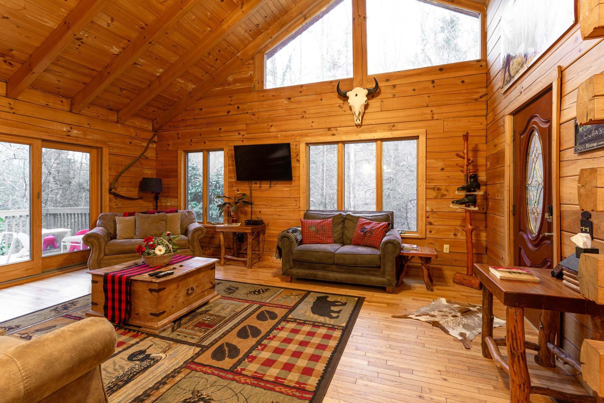 A living room in a log cabin with a couch , chairs , table and television.
