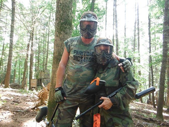 A man wearing a shirt that says paintball dictator stands next to another man