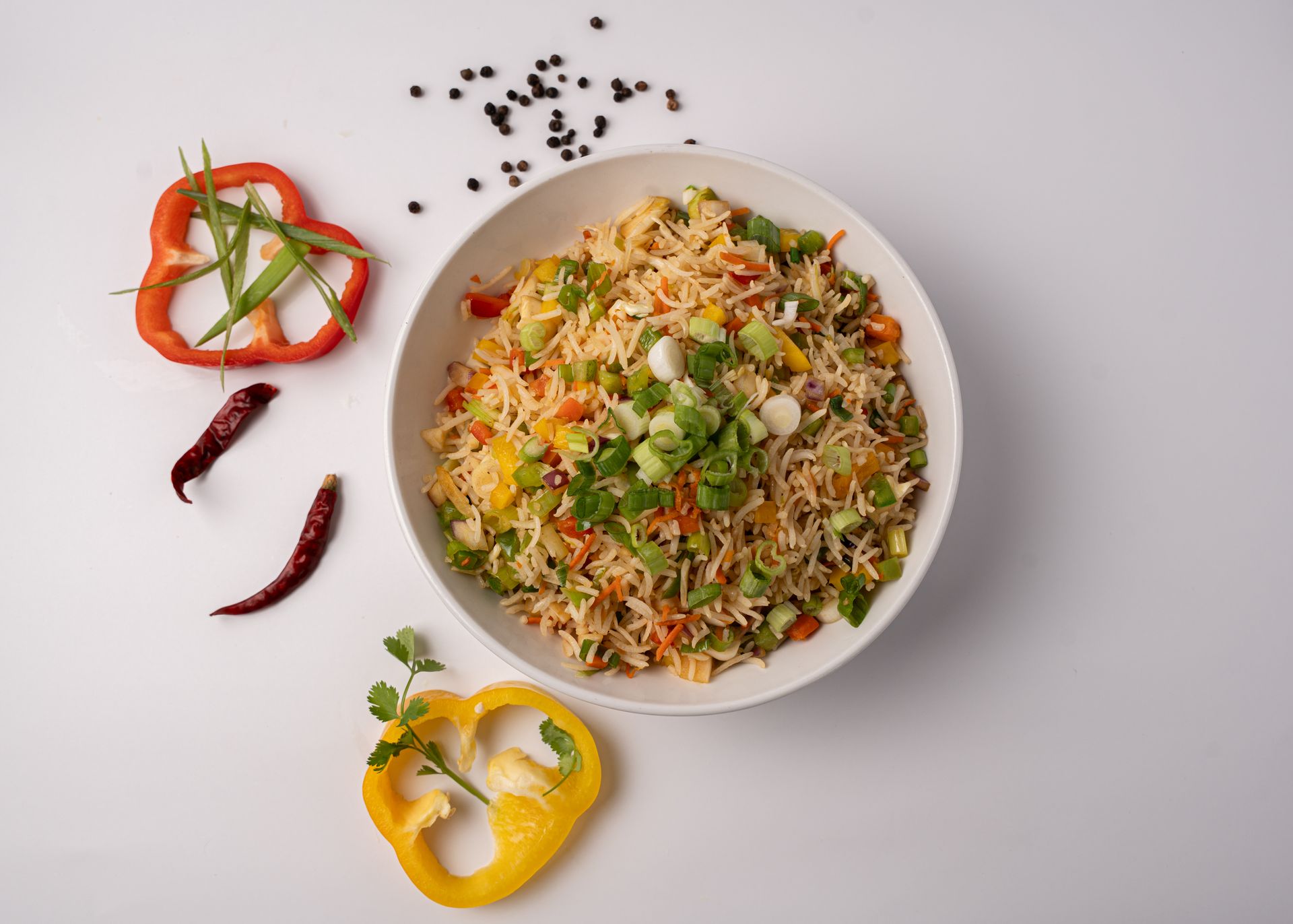 Bowl of vegetable fried rice with bell peppers and chili peppers on a white surface.