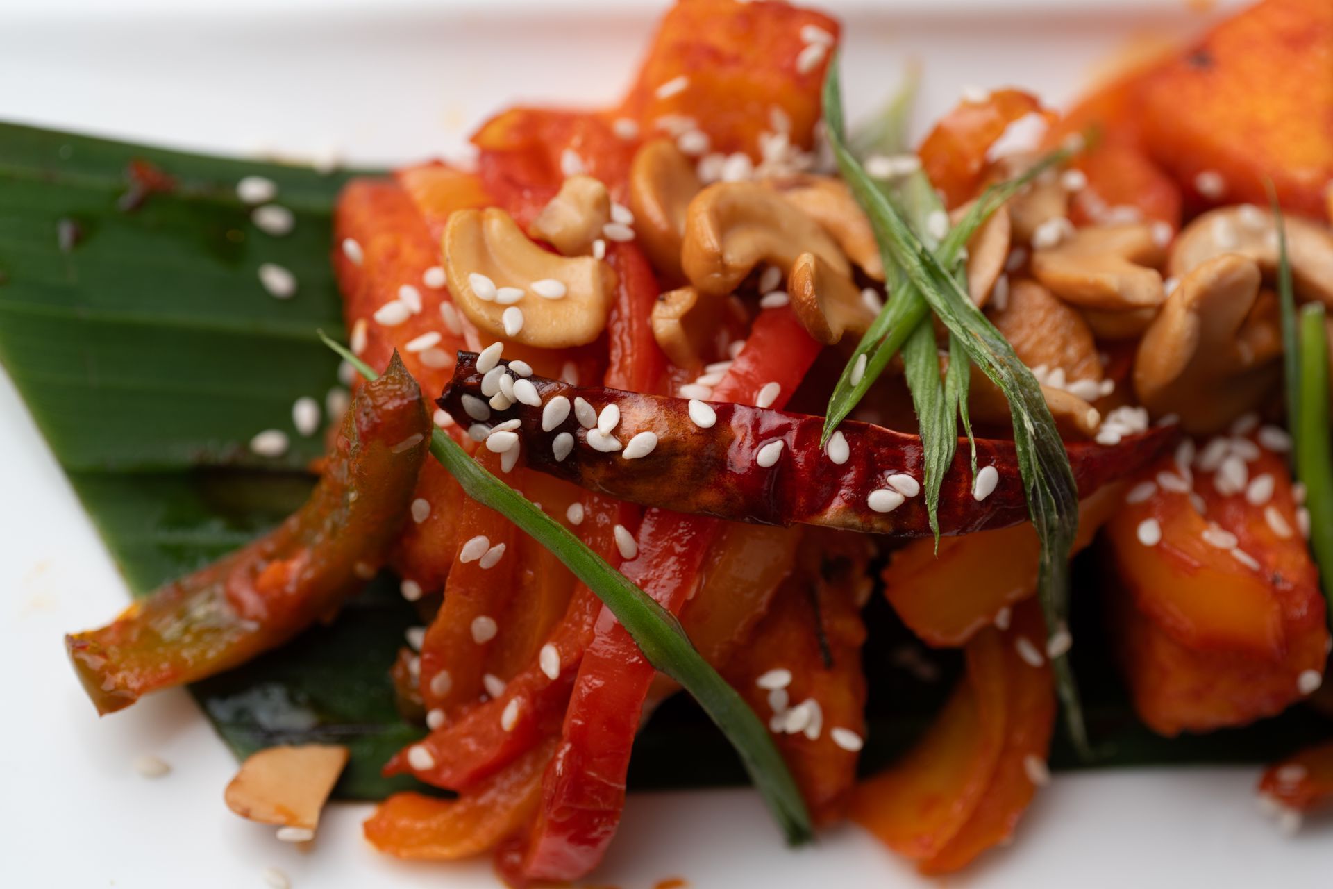 Sweet potato dish with red peppers, cashews, sesame seeds, and green onion, served on a green leaf.
