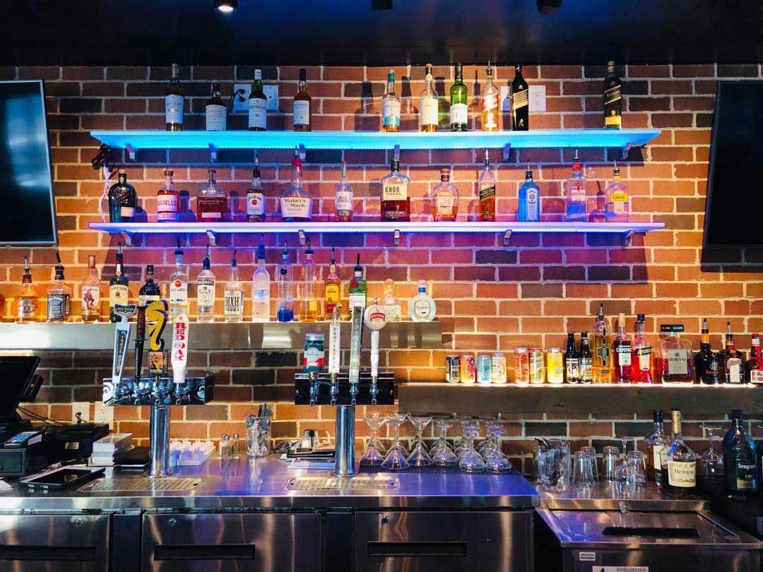 A bar with a brick wall and shelves filled with bottles of liquor.
