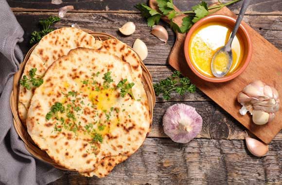 A bowl of naan bread with garlic and butter on a wooden table.