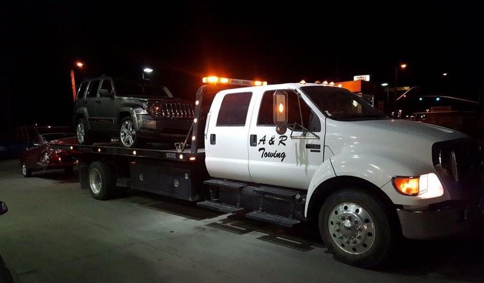 A tow truck is carrying a jeep on the back of it.