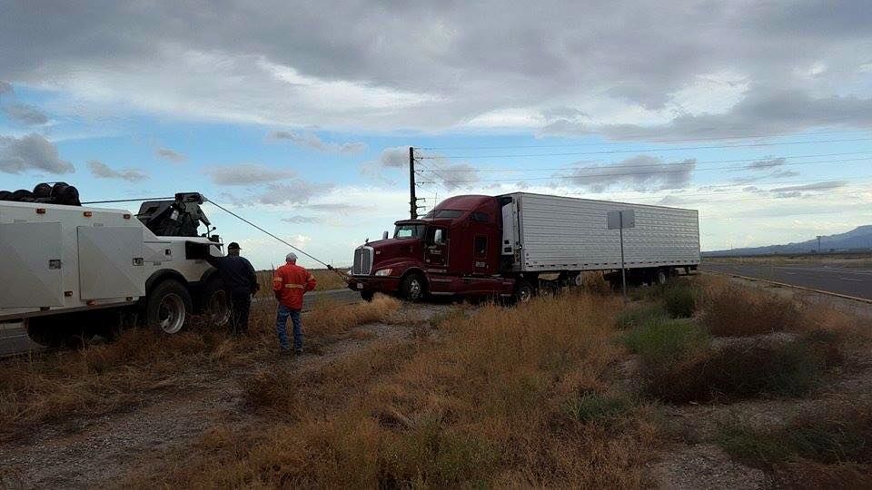 A semi truck is being towed by a tow truck in a field.