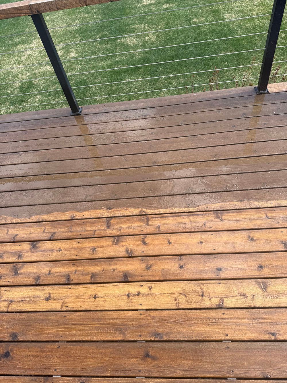 Wooden deck with black railing beside a gray building in bright sunlight