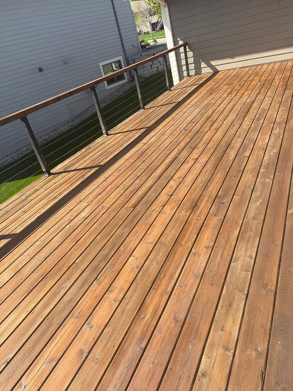 Wooden deck with black railing beside a house on a sunny day