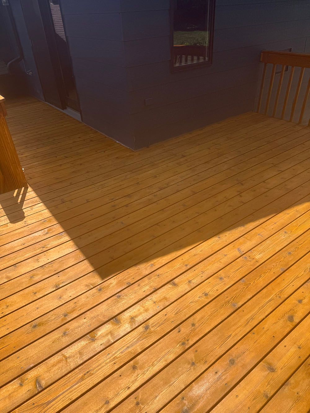 Sunlit wooden deck beside a dark building, with strong shadows across the floor.