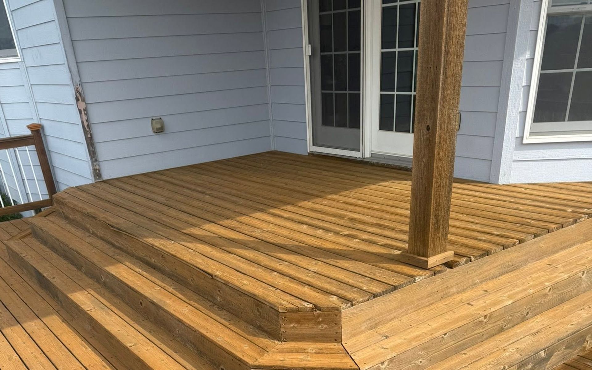 Wooden deck with steps and a railing beside a light blue house and French doors