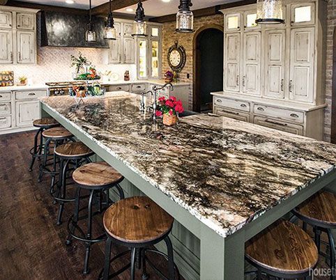 A kitchen with a large granite counter top and wooden stools.