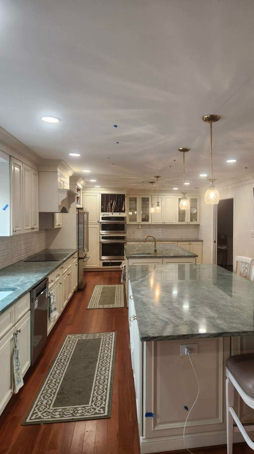 A kitchen with white cabinets , green counter tops , stainless steel appliances and a large island.