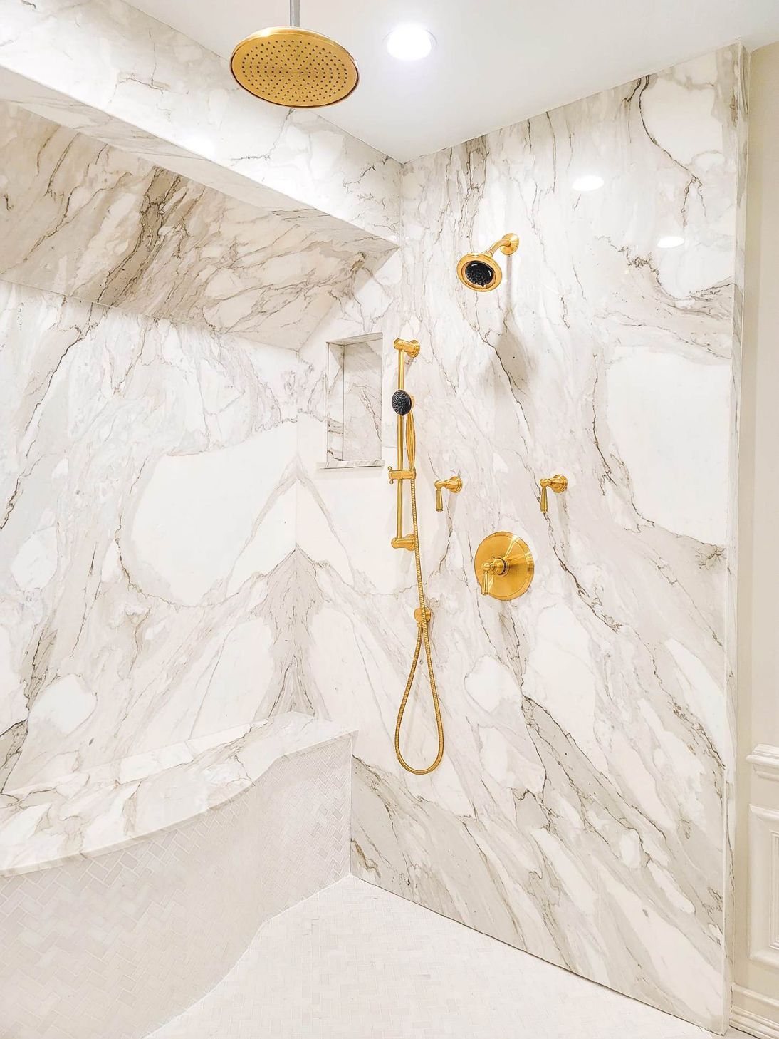 A bathroom with marble walls and a gold shower head.
