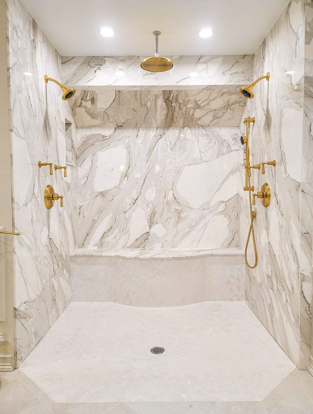 A bathroom with marble walls and a walk in shower with two shower heads.