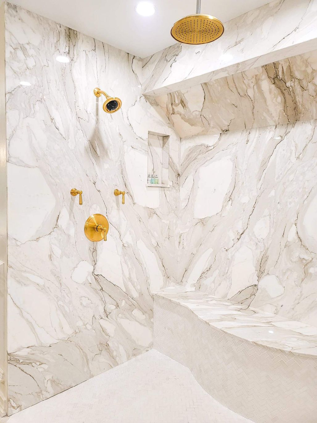 A shower with marble walls and a gold shower head.