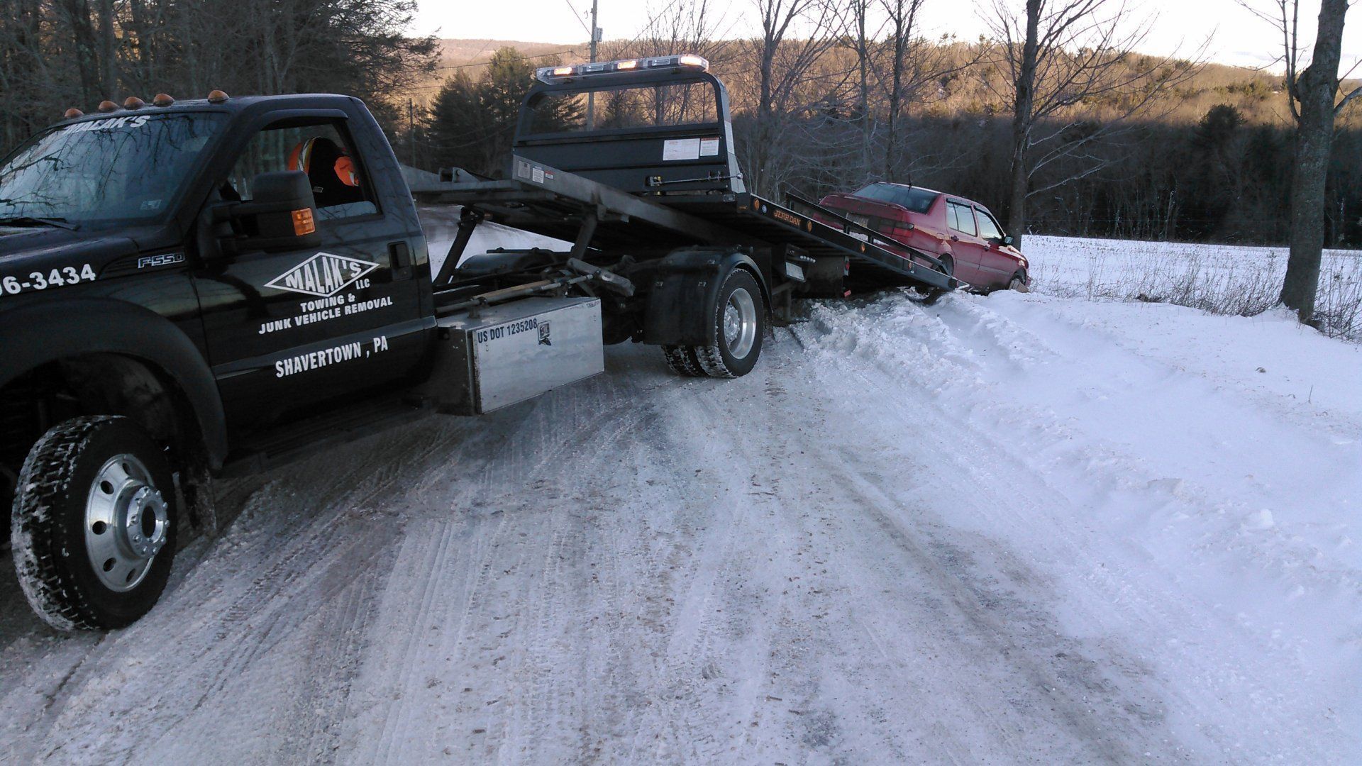 A wrecker truck is towing a car in the snow