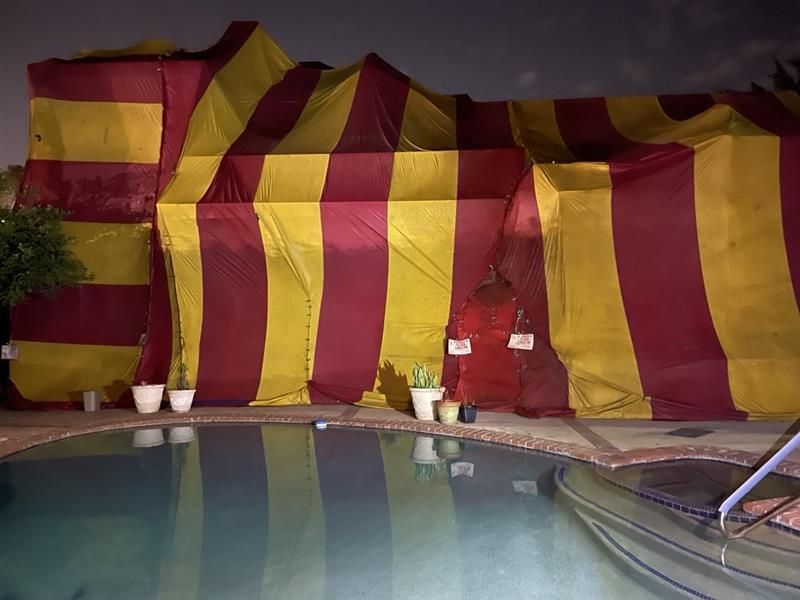 House covered in red and yellow striped tenting, next to a pool at night.