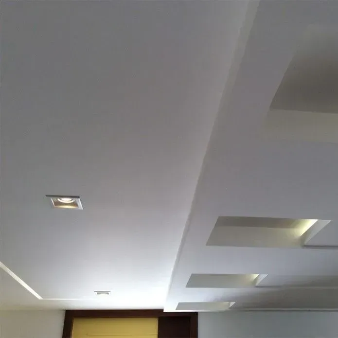 A modern white ceiling with recessed square light fixtures and a stepped architectural design.