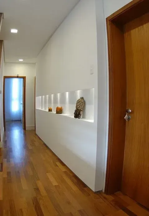A hallway with wood flooring, white walls, a built-in illuminated display shelf, and a wooden door on the right.