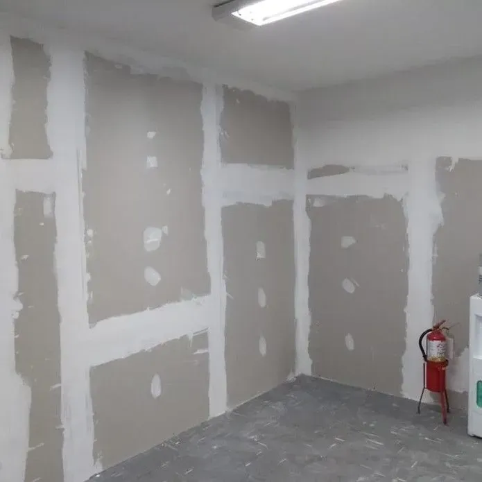 Interior corner with beige drywall sheets joined by white joint compound, a red fire extinguisher stands on the floor.