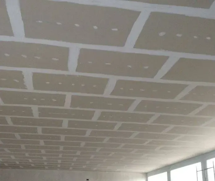 Newly installed drywall panels on a ceiling with taped seams and visible screw marks.