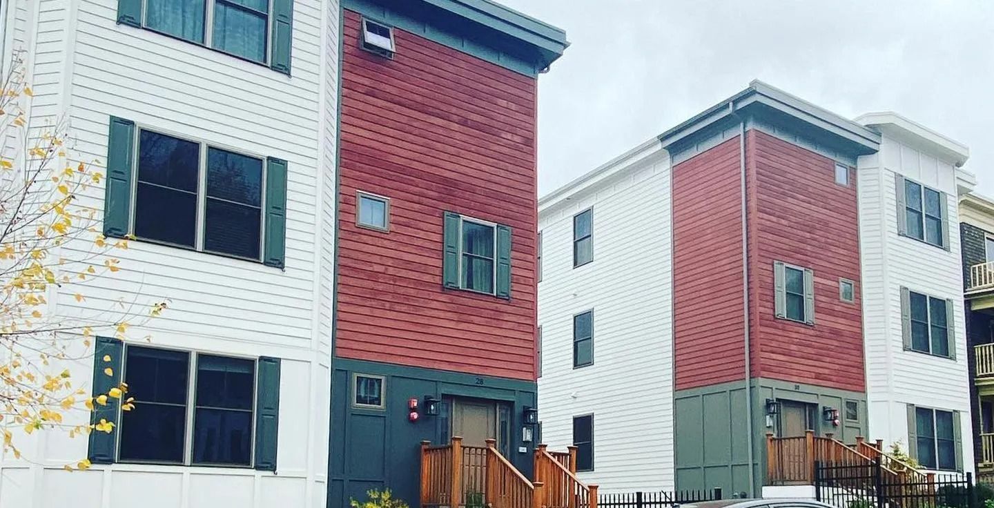 Two modern three-story apartment buildings with white siding, red brick accents, and dark green shutters.