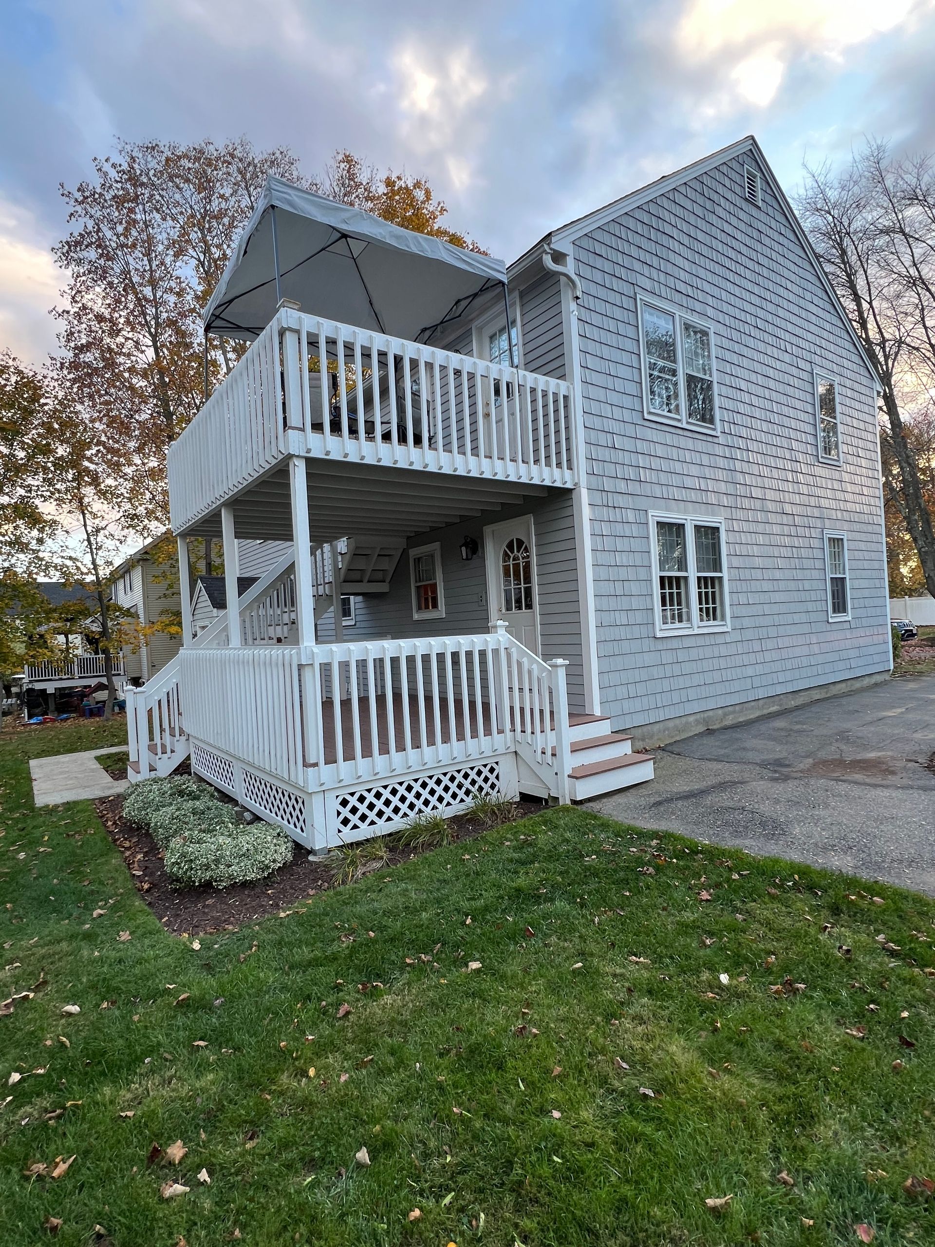 A two-story light blue house with white trim, featuring a double-decker front porch and a gravel driveway at dusk.