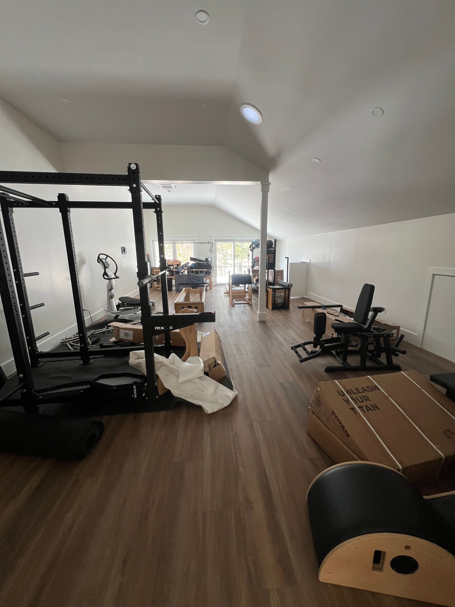 A spacious home gym with a squat rack, exercise bench, Pilates equipment, and workout gear on a wooden floor.